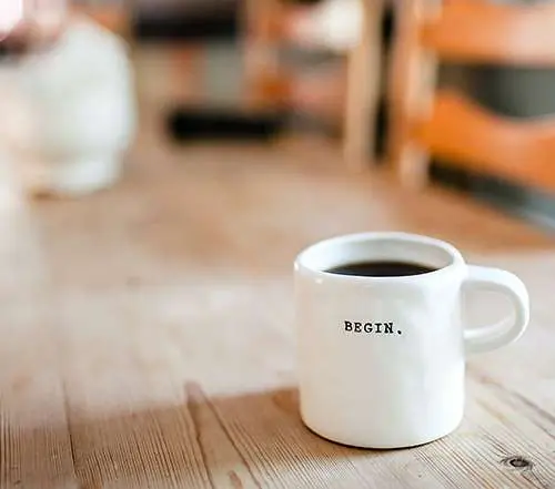 A coffee mug on a table. The coffee mug has the words "begin" written on it.