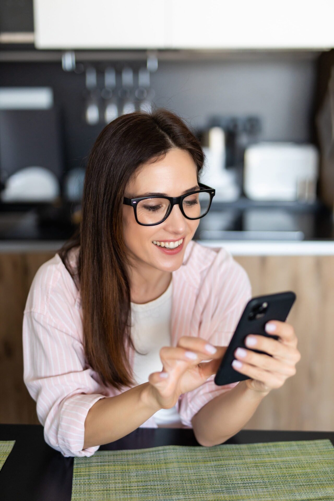 Young woman using smartphone leaning at kitchen table with coffee mug and organizer in a modern home. Smiling woman reading phone message. Brunette happy girl typing a text message. Inference based cognitive behavioral therapy